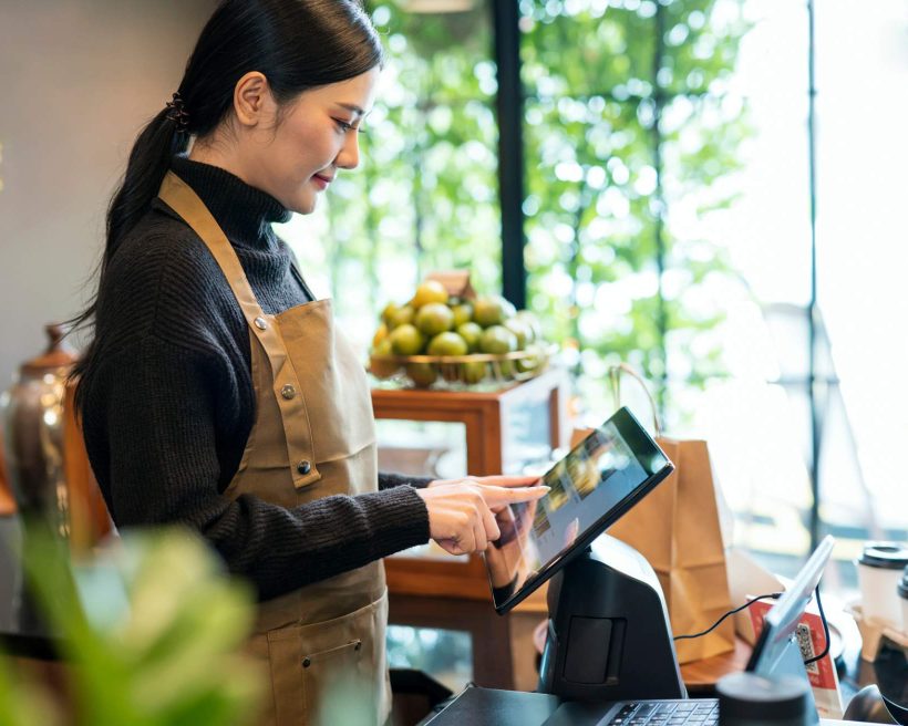 Bild einer Frau mit schwarzem Rollkragenpullover und brauner Schürze, die in einem Restaurant ein fest installiertes Tablet nutzt.