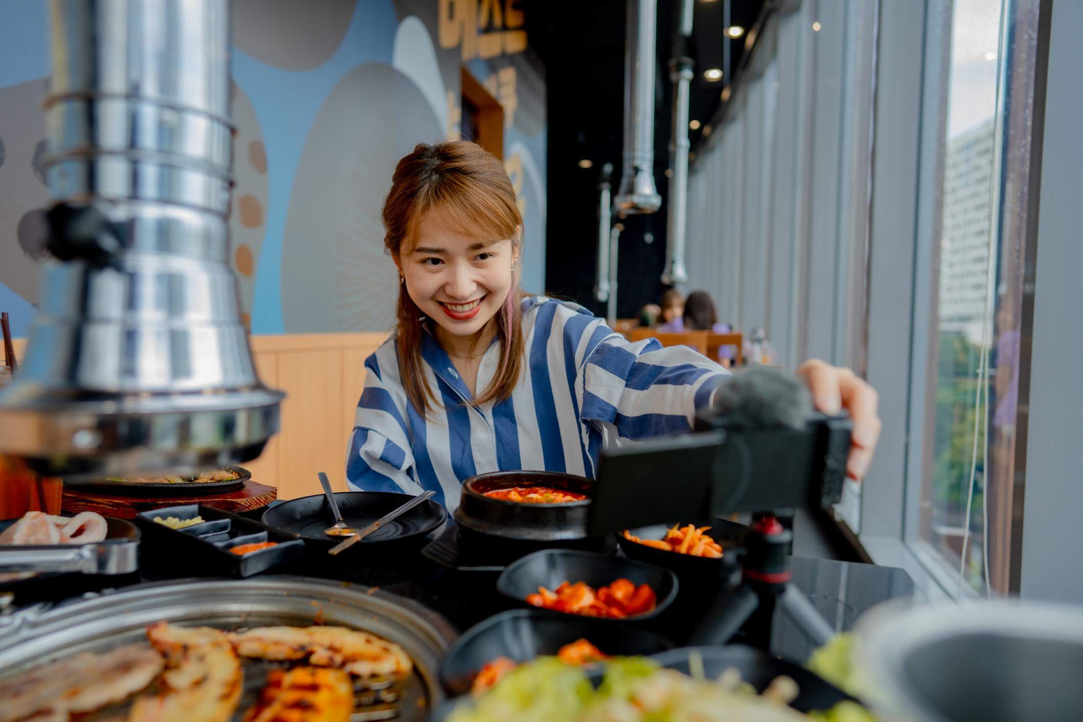 Das Bild zeigt eine Food-Influencerin, die einen Beitrag über ein Restaurant erstellt. Sie hält ein Smartphone über den Tisch, um ein Video aufzunehmen.